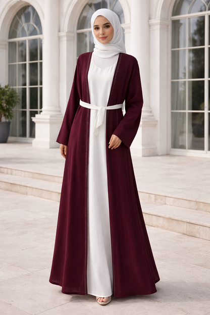 Woman wearing a burgundy and white abaya in front of a classical building.