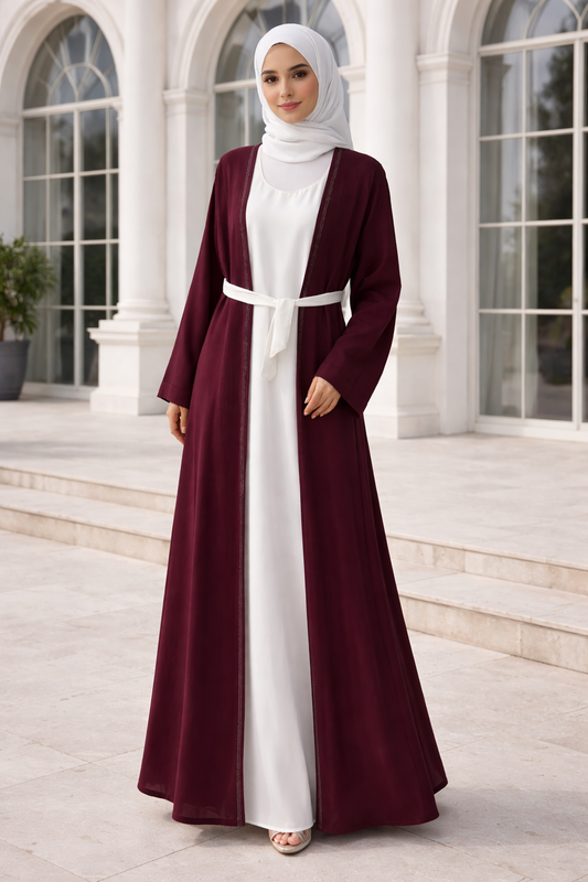 Woman wearing a burgundy and white abaya in front of a classical building.