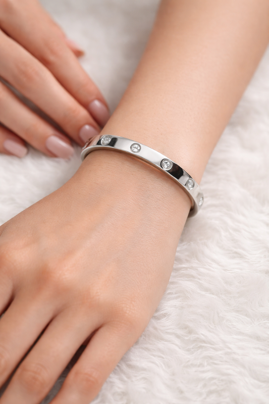 Polished silver bangle bracelet featuring alternating diamond stones and engraved screw motifs, worn elegantly on a woman’s wrist