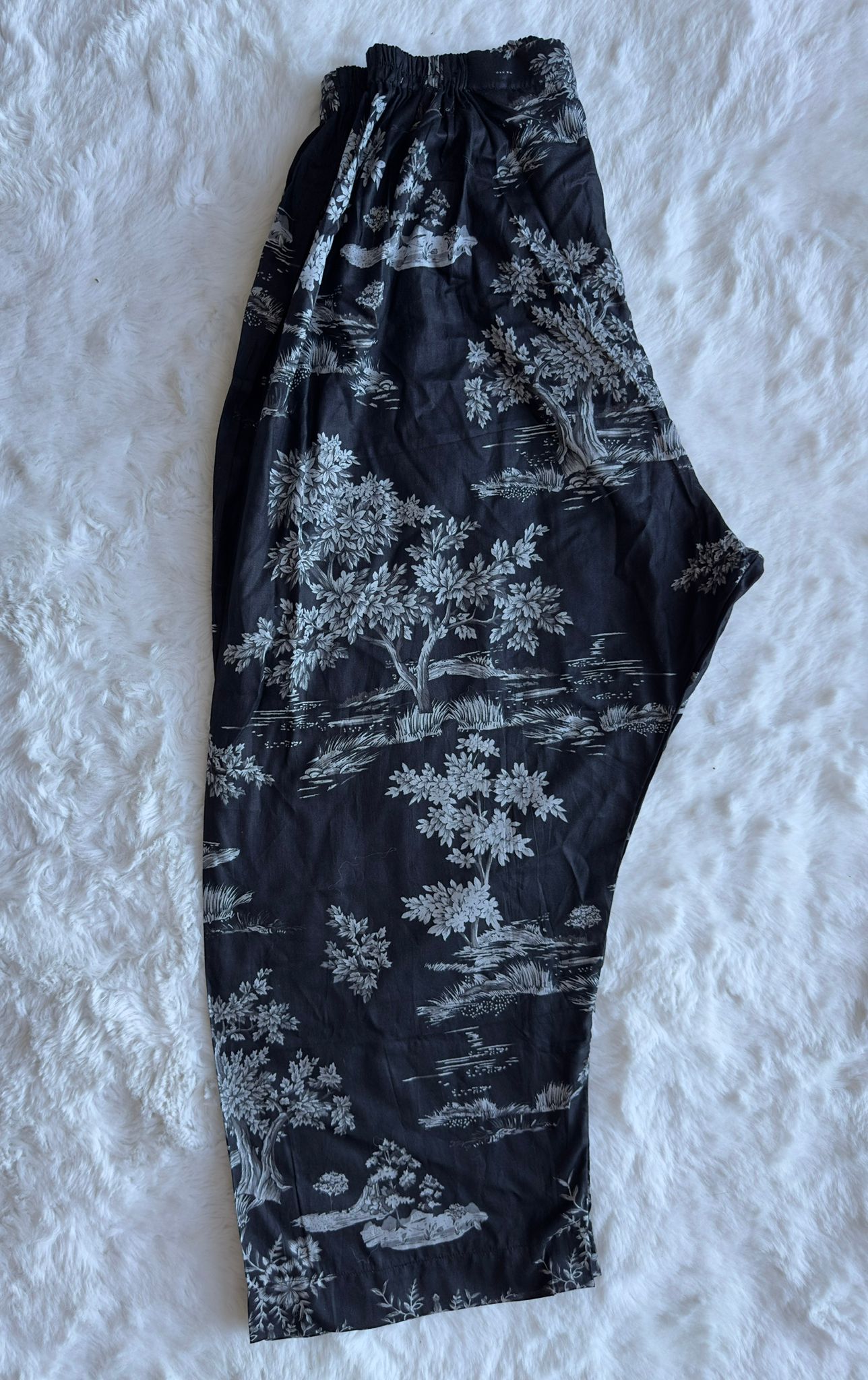 Black pants with white floral pattern on a textured white background