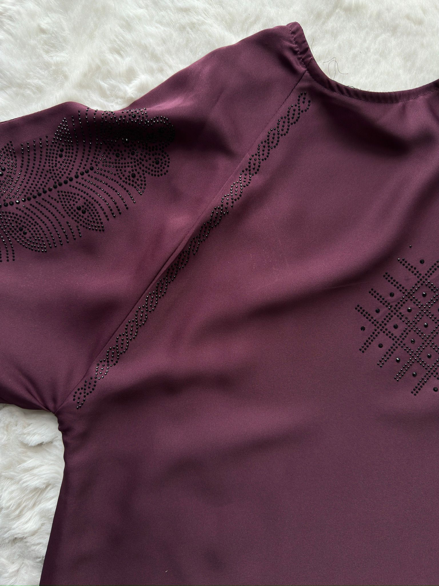 Purple garment with intricate black embroidery on a textured white background