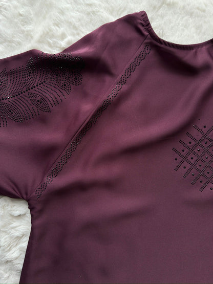 Purple garment with intricate black embroidery on a textured white background